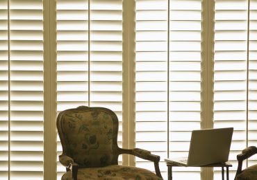 Armchair and laptop in front of domestic wooden window shutters.