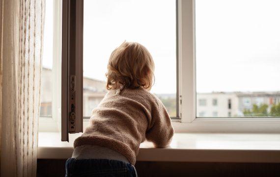 The child climbs to the window, the girl on the window sill rests on the net, the danger of falling
